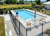 Thumbnail 8 of 9 - A pool surrounded by a black fence with a sun lounger and table.