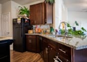 Thumbnail 1 of 9 - A kitchen with a black refrigerator and wooden cabinets.