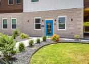Thumbnail 21 of 27 - a blue door on a brick building with a lawn and plants