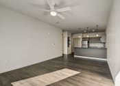 Thumbnail 17 of 26 - an empty living room with a ceiling fan and a kitchen in the background