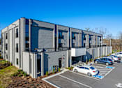 Thumbnail 12 of 23 - A modern building with a parking lot in front.