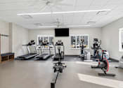 Thumbnail 11 of 26 - A spacious gym with treadmills, elliptical machines, and a fan.