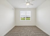 Thumbnail 22 of 26 - A room with a ceiling fan and a window overlooking a green field.