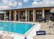 Thumbnail 14 of 26 - A pool with sun loungers and a building in the background.