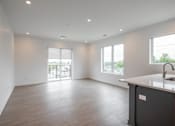 Thumbnail 14 of 23 - A spacious kitchen and living room with a wooden floor and white walls.