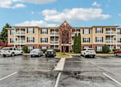 Thumbnail 56 of 58 - A parking lot in front of a large apartment building with cars parked in it.