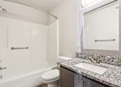 Thumbnail 21 of 35 - A bathroom with a granite countertop and a white bathtub.
