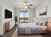 Thumbnail 1 of 61 - A bedroom with a large bed, a flat screen TV, and a balcony with a view of trees.