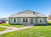 Thumbnail 15 of 35 - A small house with a grey roof and a green front.
