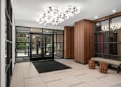Thumbnail 27 of 41 - A modern hallway with a black and white tiled floor, a black mat, and a chandelier.