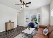 Thumbnail 3 of 16 - A living room with a brown leather couch, a wooden cabinet, a blue chair, and a ceiling fan.