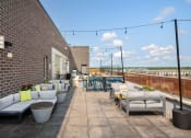 Thumbnail 15 of 45 - a rooftop terrace with couches and tables and a brick wall at Verge Apartments in St. Louis Park, MN