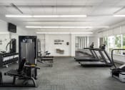 Thumbnail 20 of 45 - a gym with treadmills and other exercise equipment in a large room with windows at Verge Apartments in St. Louis Park, MN