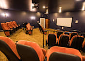 Thumbnail 28 of 64 - A row of orange chairs are arranged in front of a screen in a dark room.