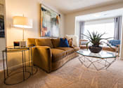 Thumbnail 19 of 64 - A living room with a brown couch, a glass table, and a plant.
