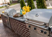 Thumbnail 54 of 64 - A silver grill with a vase of yellow flowers on top of it.