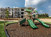 Thumbnail 51 of 64 - A playground with a green slide in front of apartment buildings.
