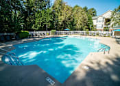 Thumbnail 27 of 58 - A swimming pool surrounded by trees and a building in the background.