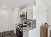 Thumbnail 5 of 16 - 2 Bedroom Townhomes In Blue Springs, MO - Chapman Ridge Townhomes - A Kitchen Features Granite Countertops, White Cabinets, Stainless Steel Oven, Vinyl Plank Flooring, And A Small Potted Plant.