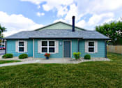 Thumbnail 5 of 35 - 2-Bedroom Apartments in St. Vincent Greenbriar, Indianapolis, IN - The Jameson - Outdoor View of a Single-Story House with Blue Siding, Door, Windows, Plants, and Lawn.