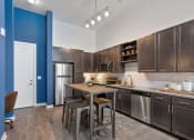 Thumbnail 87 of 95 - Two-Bedroom Apartments inGermantown, Nashville, TN -Peyton Stakes - Kitchen withHardwood-Inspired Flooring,Stainless Steel Appliances, DarkWooden Cabinetry, White SubwayTile Backsplash, Granite Countertops, Kitchen Island with Bar Stools, and Blue Accent Wall.