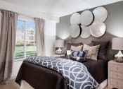 Thumbnail 15 of 25 - Ardenne Apartments bedroom with large windows, beigh drapes and queen sized bed with brown and blue bedding