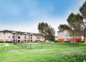 Thumbnail 10 of 25 - Ardenne Apartments grassy, fenced in dog park with community buildings behind it.