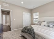 Thumbnail 8 of 11 - Senior Housing in Belton, MO - Traditions Villas 55+ - Bedroom with Carpet Flooring, High Ceiling, Light Fixtures, Large Bed, Dresser, Window with Blinds, and Doorway.