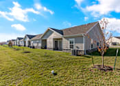 Thumbnail 4 of 11 - Two-Bedroom Senior Townhomes in Belton, MO - Traditions Villas 55+ - A Lawn Fronting a Row of Houses, and a Tree.