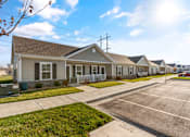 Thumbnail 2 of 11 -  Dog-Friendly Senior Townhomes in Belton, MO - Traditions Villas 55+ - An Off-Street Parking Area Fronting a Row of Houses with Fences and Yards.