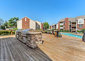 Thumbnail 30 of 77 - A wooden deck with a stone fireplace and a pool in the background.
