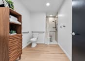 Thumbnail 49 of 53 - A bathroom with a toilet, a wooden cabinet, and a shower.