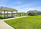Thumbnail 14 of 16 - Townhomes In Blue Springs, MO - Chapman Ridge Townhomes - A Park With Concrete Walkways, Picnic Tables, Playground Area, Lush Green Lawn, And Clear Blue Sky.
