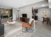 Thumbnail 6 of 30 - A living room with a grey couch, a brown chair, and a white coffee table.