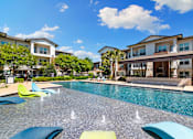 Thumbnail 15 of 47 - A pool with blue and green lounge chairs in front of apartment buildings.