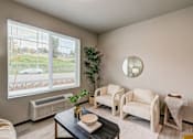 Thumbnail 5 of 25 - A living room with a large window, a couch, a chair, a coffee table, and a potted plant.