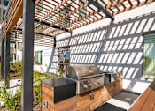 Thumbnail 19 of 43 - A modern outdoor kitchen with a grill and a pergola.