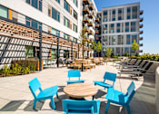 Thumbnail 17 of 43 - A patio with blue chairs and tables in front of a building.