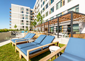 Thumbnail 16 of 43 - A sunny day at the rooftop pool with blue lounge chairs and a wooden pergola.
