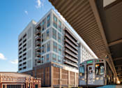 Thumbnail 39 of 43 - A train is on a track under a bridge next to a building.