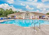 Thumbnail 2 of 20 - A large swimming pool in front of a building with a blue sky and clouds in the background.