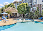 Thumbnail 2 of 27 - A swimming pool with a slide and sun loungers in front of apartment buildings.
