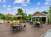 Thumbnail 17 of 30 - A patio with tables and chairs is surrounded by trees.