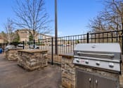 Thumbnail 21 of 30 - A BBQ grill is on a patio with a stone wall and a black fence.