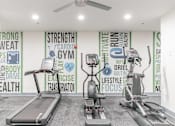 Thumbnail 11 of 30 - A gym with treadmills, elliptical machines and a wall of fitness related words.