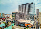 Thumbnail 1 of 18 - A modern hotel building is in the background of a cityscape.