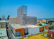 Thumbnail 2 of 18 - A modern glass building stands out in a cityscape.