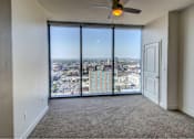 Thumbnail 7 of 18 - A room with a ceiling fan and a view of the city.