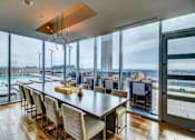 Thumbnail 14 of 18 - A modern dining room with a long wooden table and chairs, a chandelier, and a view of the outdoors through large windows.