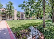 Thumbnail 8 of 25 - a green lawn with trees and a sidewalk in front of an apartment building